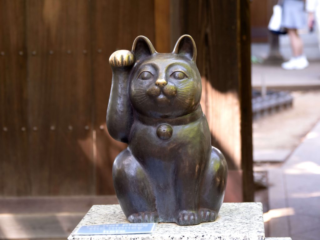 Schwarze Maneki-neko-Figur mit erhobener Pfote vor einem Hauseingang.